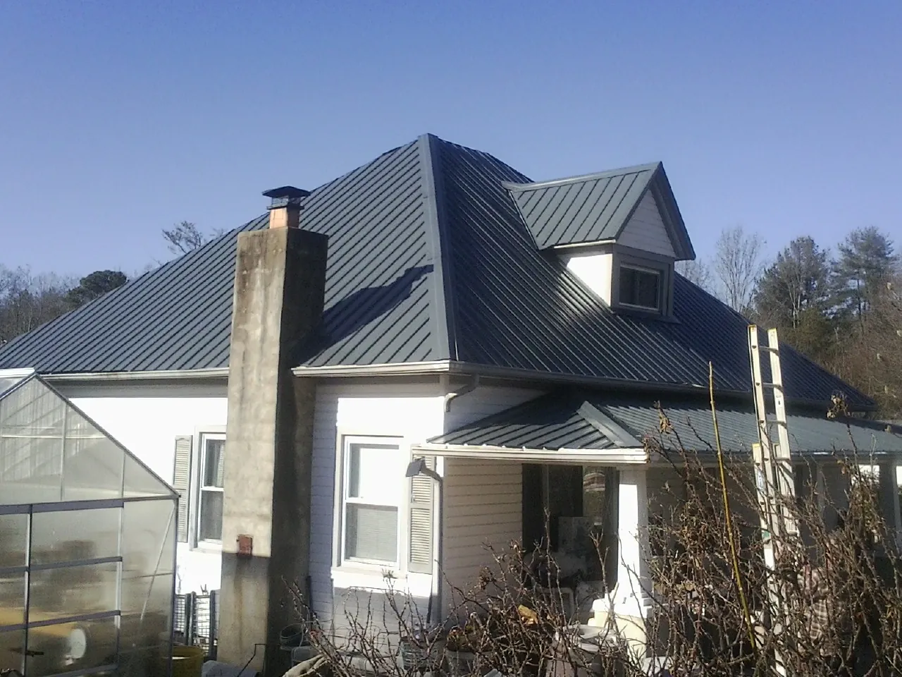 Dark blue standing seam metal roof on a white farmhouse with dormer — Slate & Tile Roof Repair by Roofing Brothers in Garrett