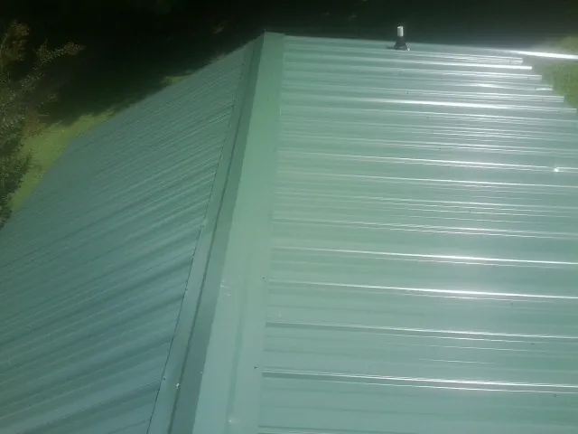 New green metal panels meeting at the ridge of a roof — Flat Roof Repair work by our crew in Garrett